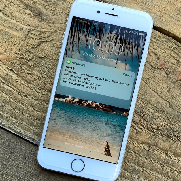 Vit mobil som på skärmen visar ett sms från HMAB med påminnelse om hämtning