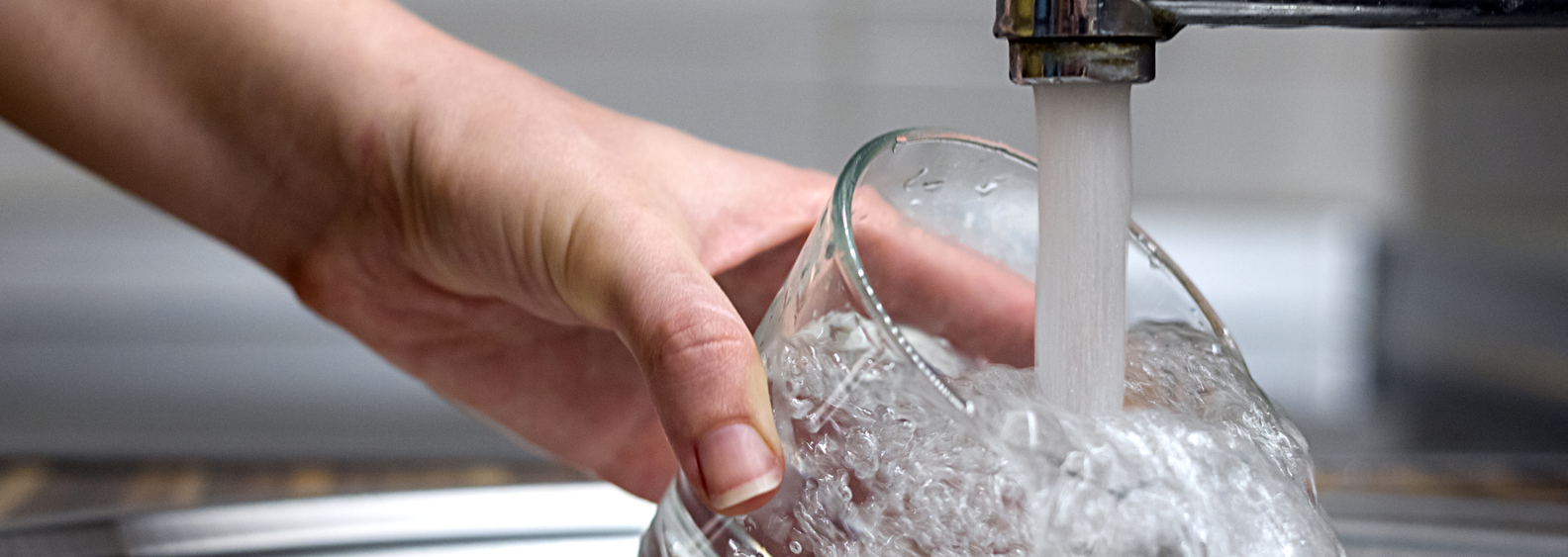 Female hands pouring water in glass cup from a kitchen faucet. Woman hand's filling the glass of water. Filling glass of water from stainless steel kitchen faucet